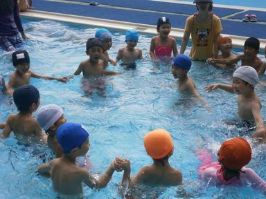 大きなプールで子供たちがそれぞれの手をつなぎ輪になっている様子の写真