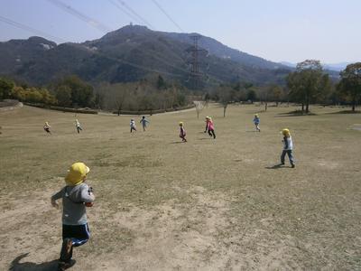10名の子供たちが、晴れの日中、山が見える広場で走り回る写真